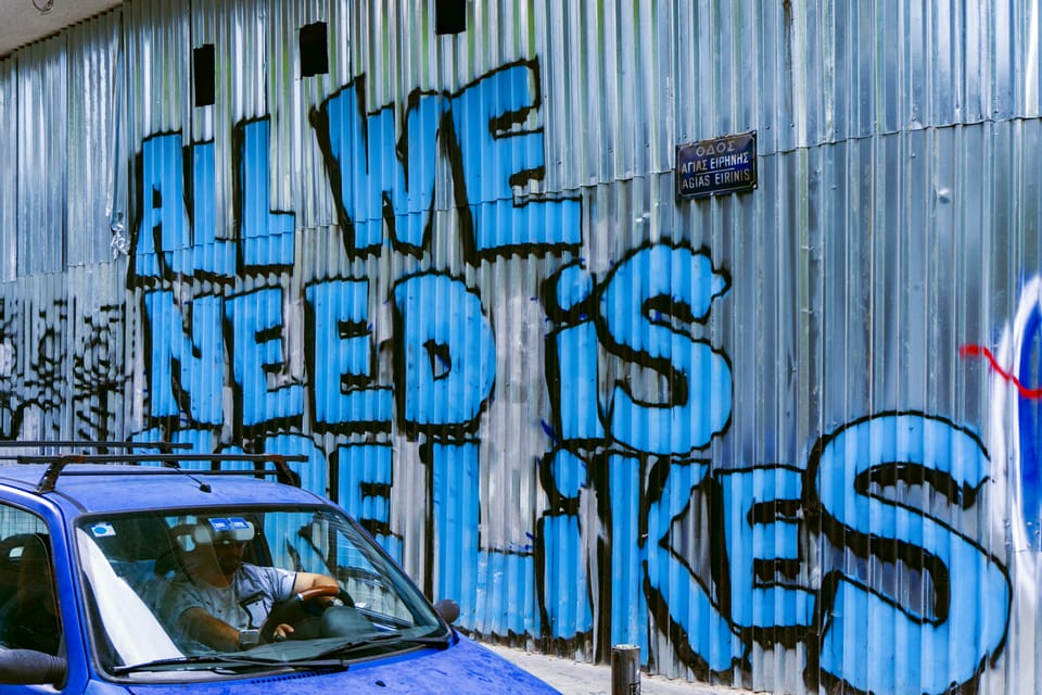 Graffiti on a corrugated iron fence in Greece which reads: "All we need is more likes"