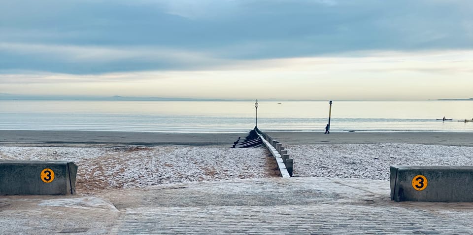 A view out to the sea from Portobello beach in Edinburgh on a winter's day - the sand is slightly frozen, and the groin stretches into a calm, sun-kissed bay